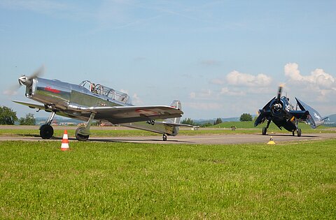 Pilatus P-2 rollt zum Start und dahinter mit gefalteten Flügeln der Grumann.