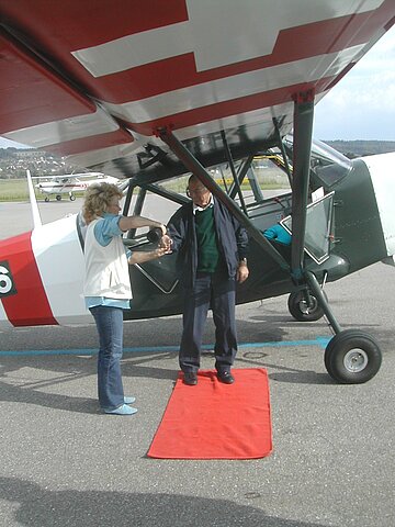 Gisela empfängt den Neuankömmling (Stinson) und den Piloten, Hansruedi mit einem Glas Champagner.